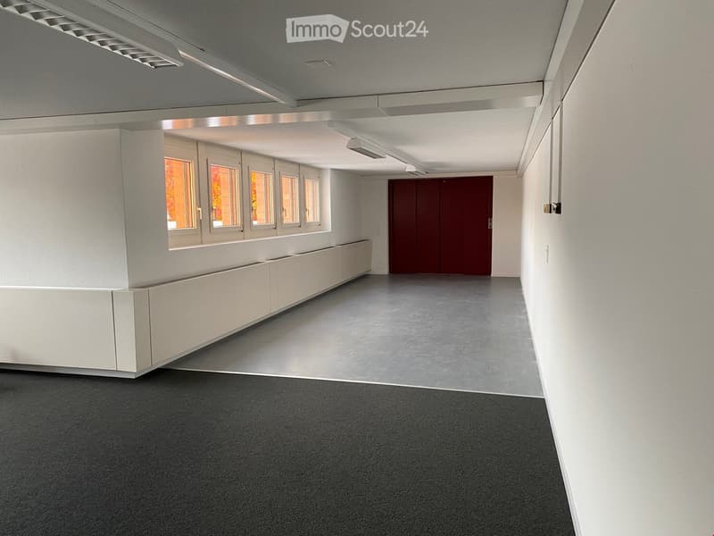 Empty room with white walls, gray floor, built-in storage along the walls, and red double doors.