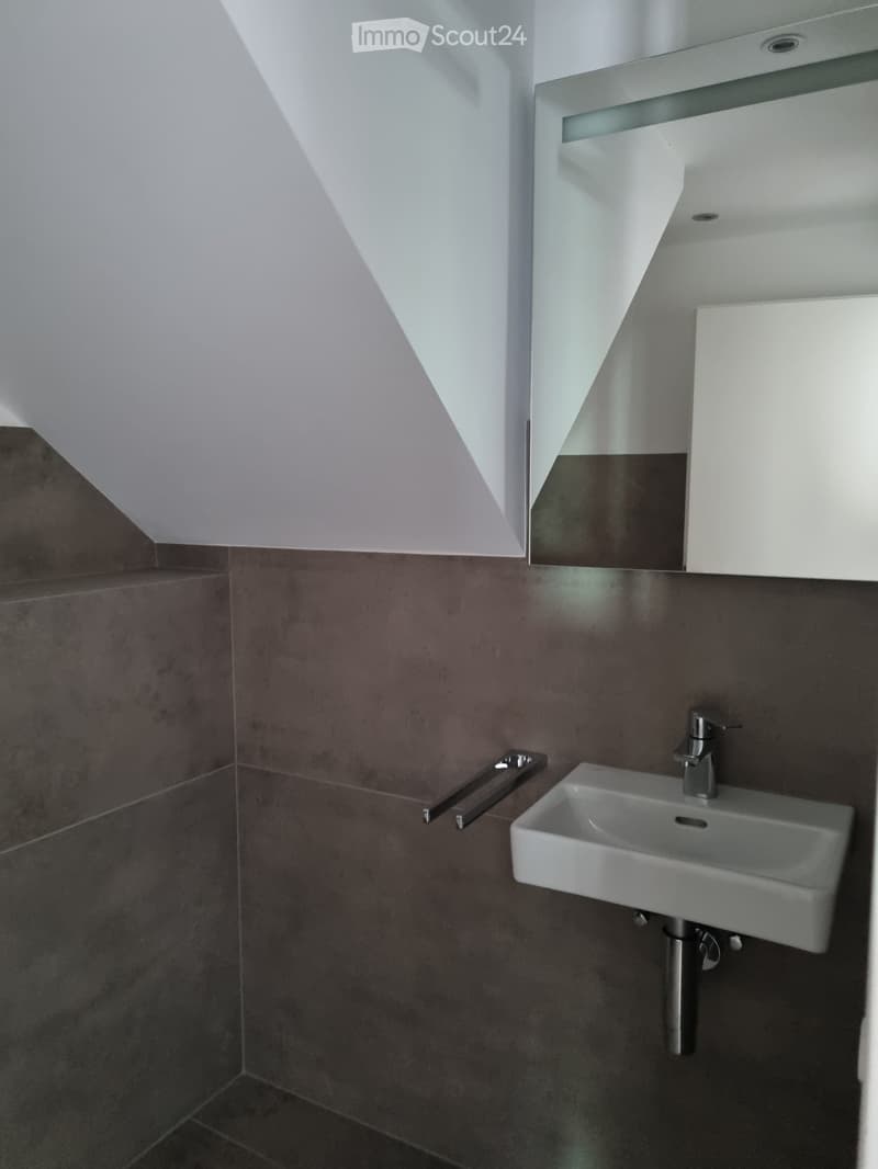 gray tiled walls, white sink, chrome faucet, mirror mounted on wall, sloped ceiling
