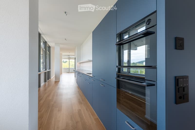 Kitchen. Modern kitchen with blue cabinets, wooden flooring, and a built-in oven. The space is bright with large windows and a sleek design.