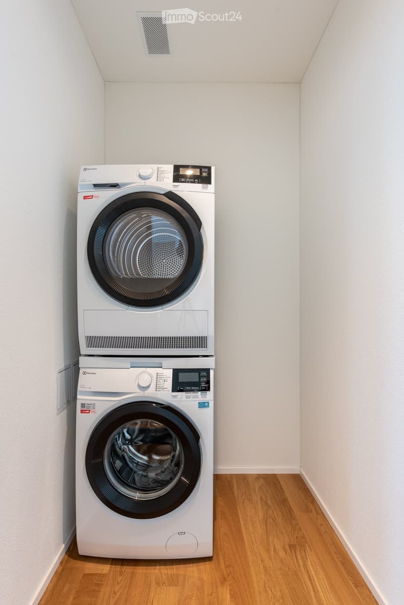 Unfurnished Room. Empty room with wooden flooring and white walls, featuring a stacked washer and dryer unit in the corner.