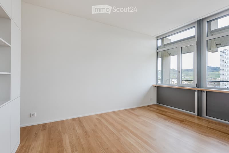 Unfurnished Room. Empty room with light wooden flooring, white walls, and large windows offering a view of the city and landscape.