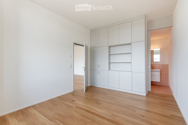 Unfurnished Room. Empty room with light wooden flooring and white walls, featuring built-in white cabinetry and open shelving, with a doorway leading to a small bathroom.