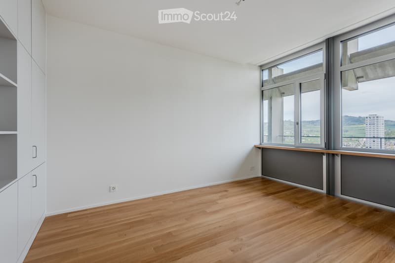 Empty room with light wooden flooring, white walls, and large windows offering a view of the landscape.