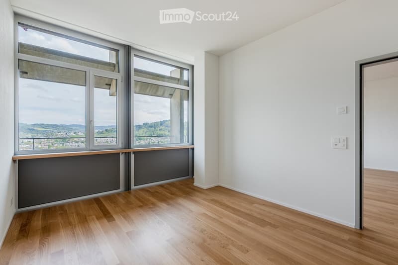 Empty room with wooden flooring, large windows offering a scenic view, and white walls.