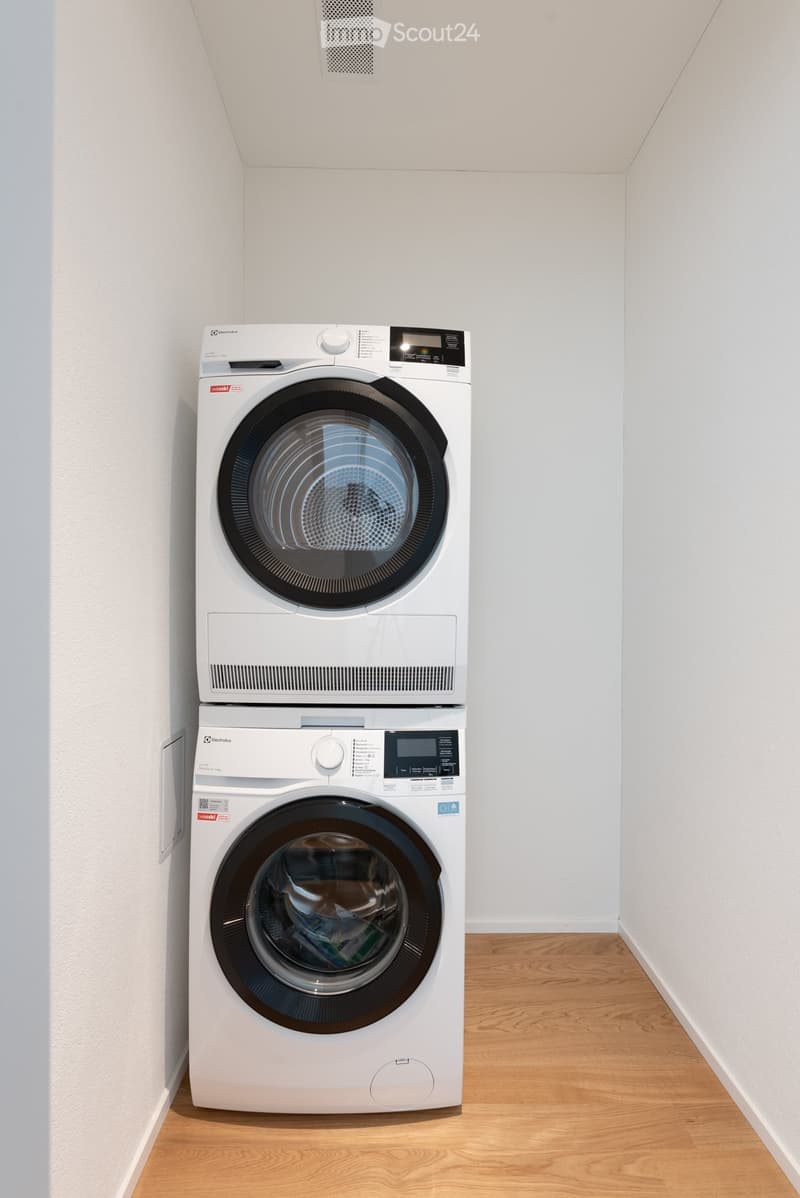 A modern, compact bathroom with a white washing machine and dryer stacked vertically, featuring a sleek design and digital control panels.