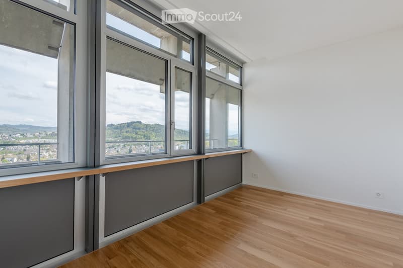 Empty room with wooden flooring, large windows offering a scenic view, and a wooden shelf along the wall.
