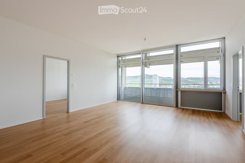 Empty room with wooden flooring, large windows, and a sliding glass door leading to a balcony.