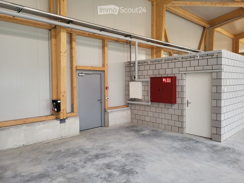 wide empty room, concrete floor, white walls, red safety box, two doors