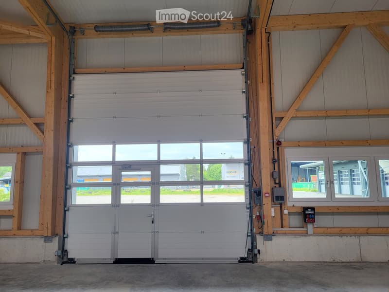 Large white garage door with windows, wooden beams on walls, gray floor, white wall panels