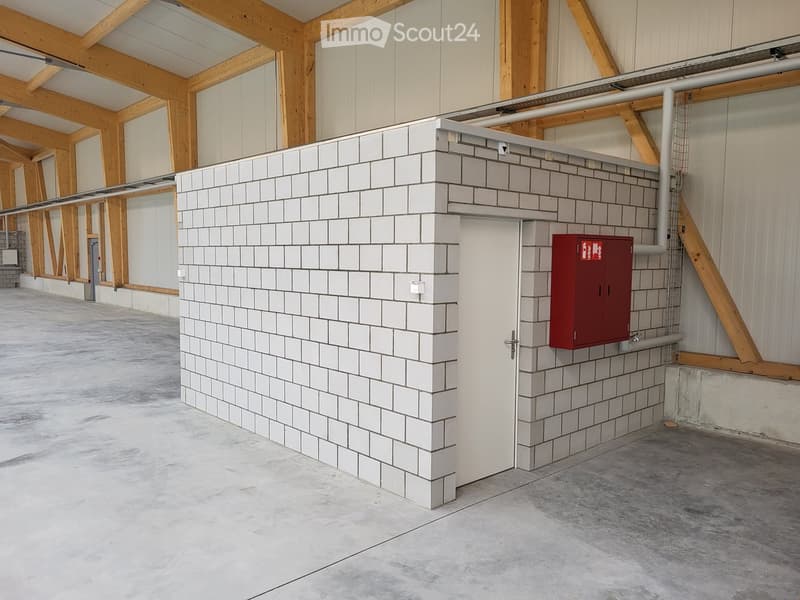 Interior of a storage building with white tiled wall, metal door, and red fire extinguisher box