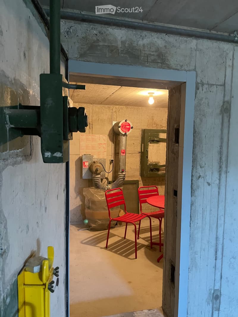 Small room, concrete walls, red chairs, red table, yellow object, pipes, machinery