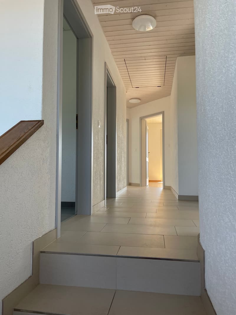The hallway has white walls, wooden handrails, wooden ceiling, and tiled flooring.