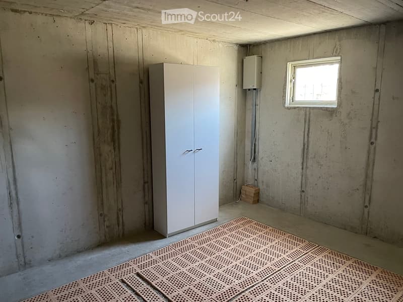Basement room with white wall, concrete floor, small window, white cabinet, empty room.