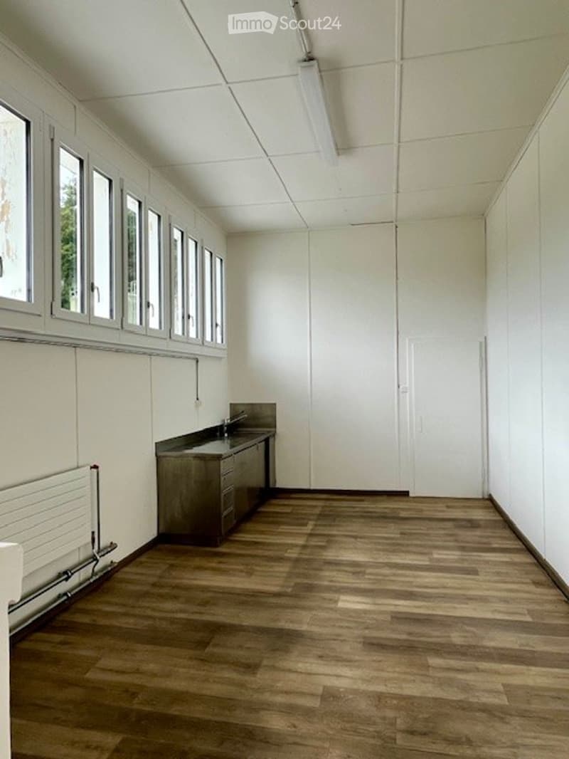 Empty room with wooden floors, white walls, a countertop, and windows.