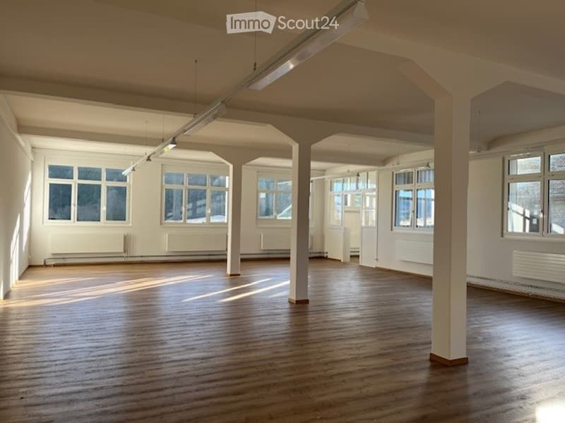 Spacious room, hardwood floor, white walls, fluorescent ceiling lights, large windows