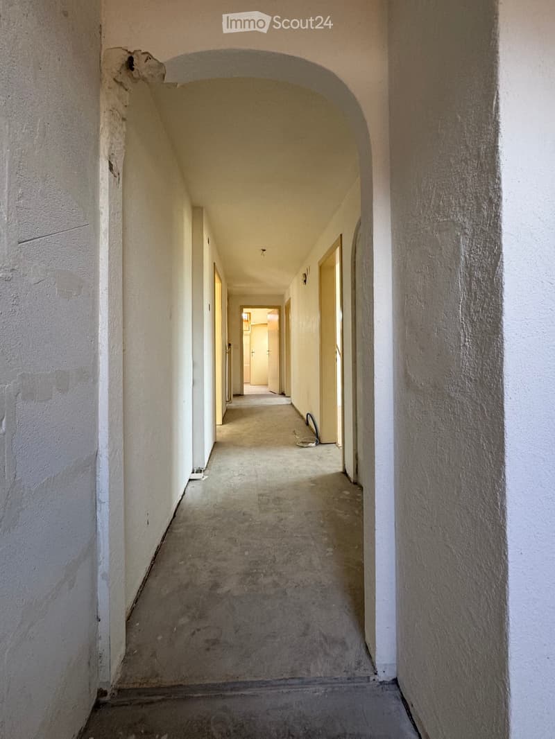 Long corridor, white walls, concrete floor, yellow door at the end