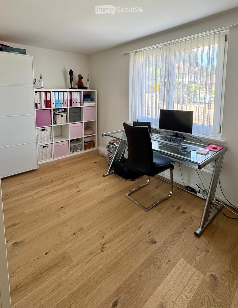 empty office, glass desk, black chair, computer monitor, keyboard, mouse, organized bookshelf, various storage boxes, clean hardwood floor, large window with white blinds