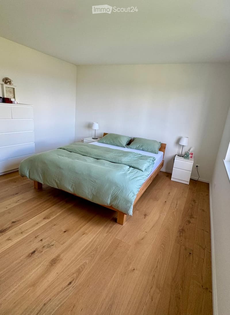 white walls, wooden floor, double bed with teal bedding, bedside tables with lamps, small cabinet, side window