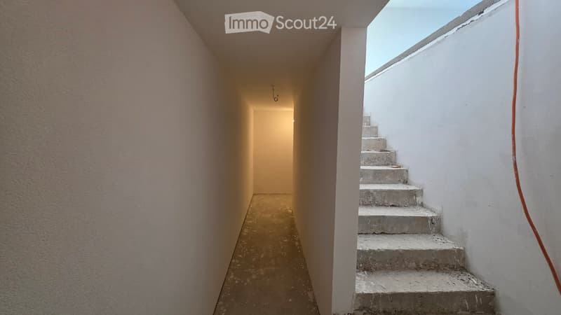 Corridor with concrete floor, white walls, concrete stairs, and a light at the end.