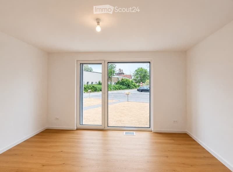 Empty room with light-colored walls, wooden flooring, and large sliding glass doors leading to an outdoor area.