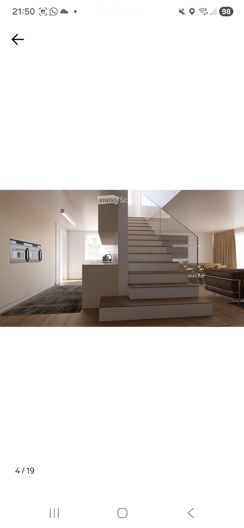 Modern, open-plan living and dining area with a staircase leading to an upper level. Features a sleek, dark-toned sofa, a minimalist kitchen with integrated appliances, and a dining table with chairs.