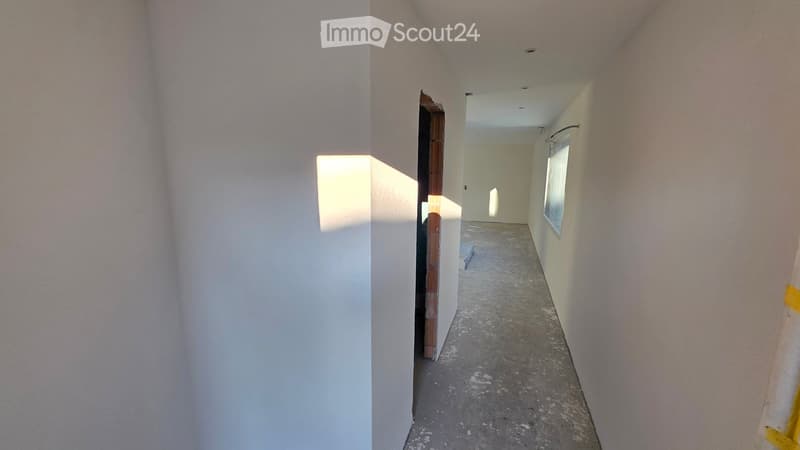 Empty hallway with white walls, concrete floor, small window, open door