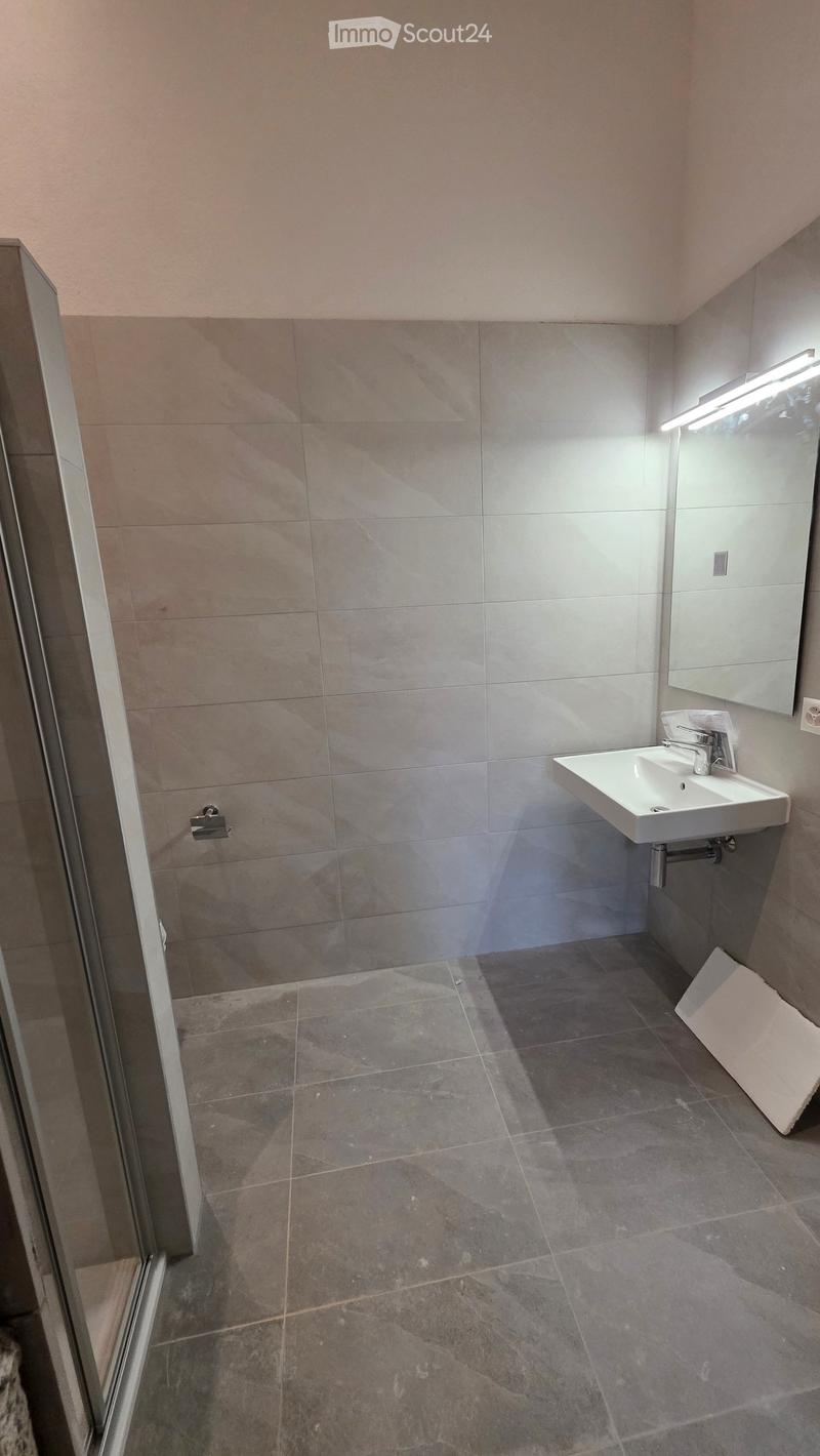 Modern bathroom with grey tiled walls and floor, white sink, mirror, and faucet.
