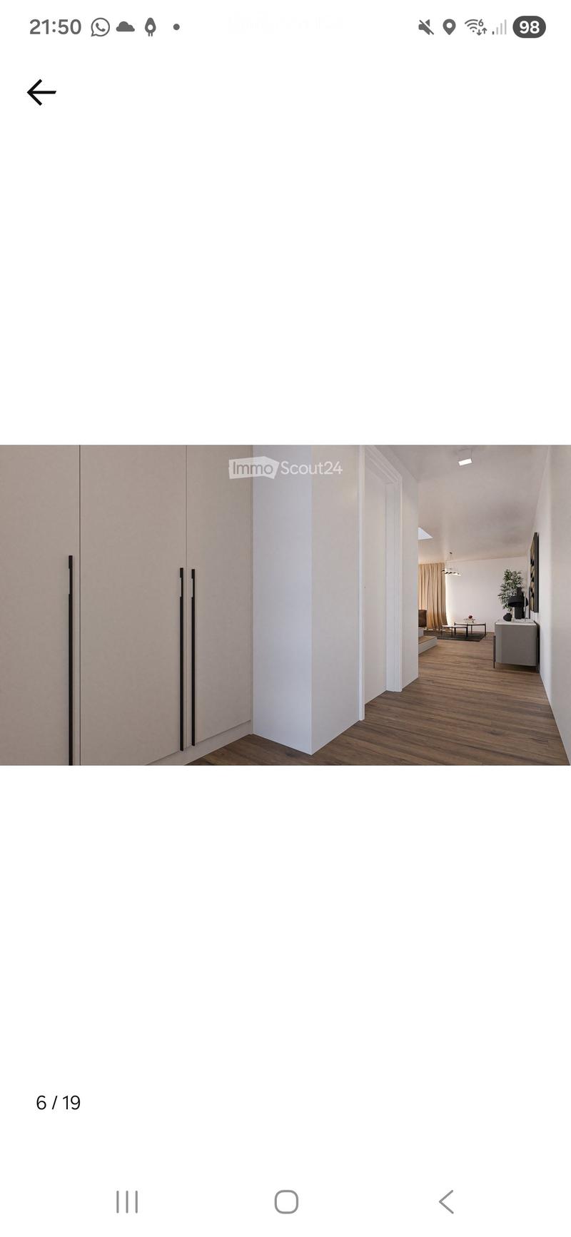A modern hallway with light-colored walls, wooden flooring, and a large open space leading to another room.