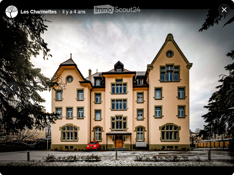 Large yellow building, multiple windows, brick foundation, red car parked