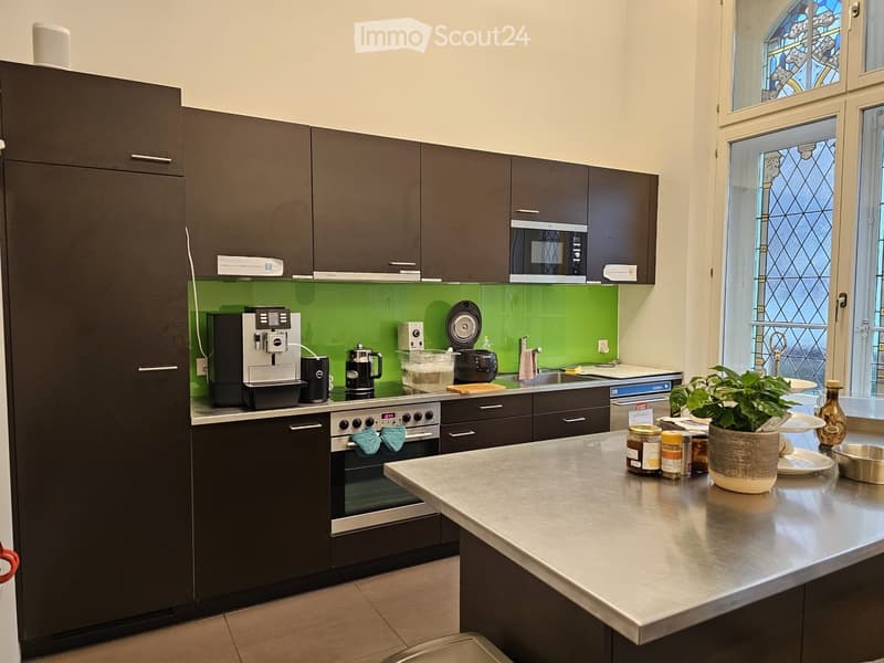 Modern kitchen with stainless steel island, oven, coffee maker, microwave, green wall, large windows, stainless steel refrigerator
