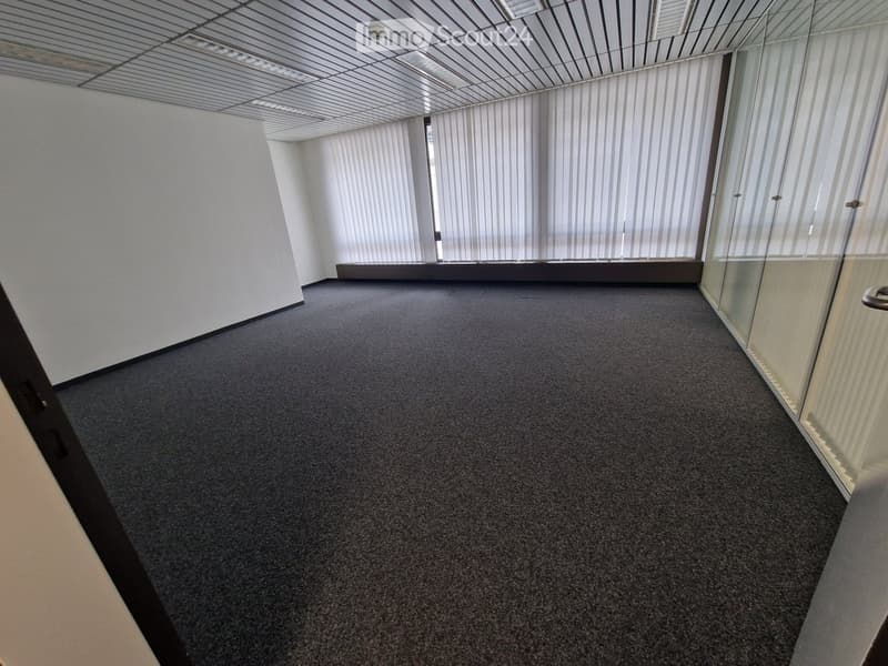 Empty room with white walls, gray carpet, large windows, security camera
