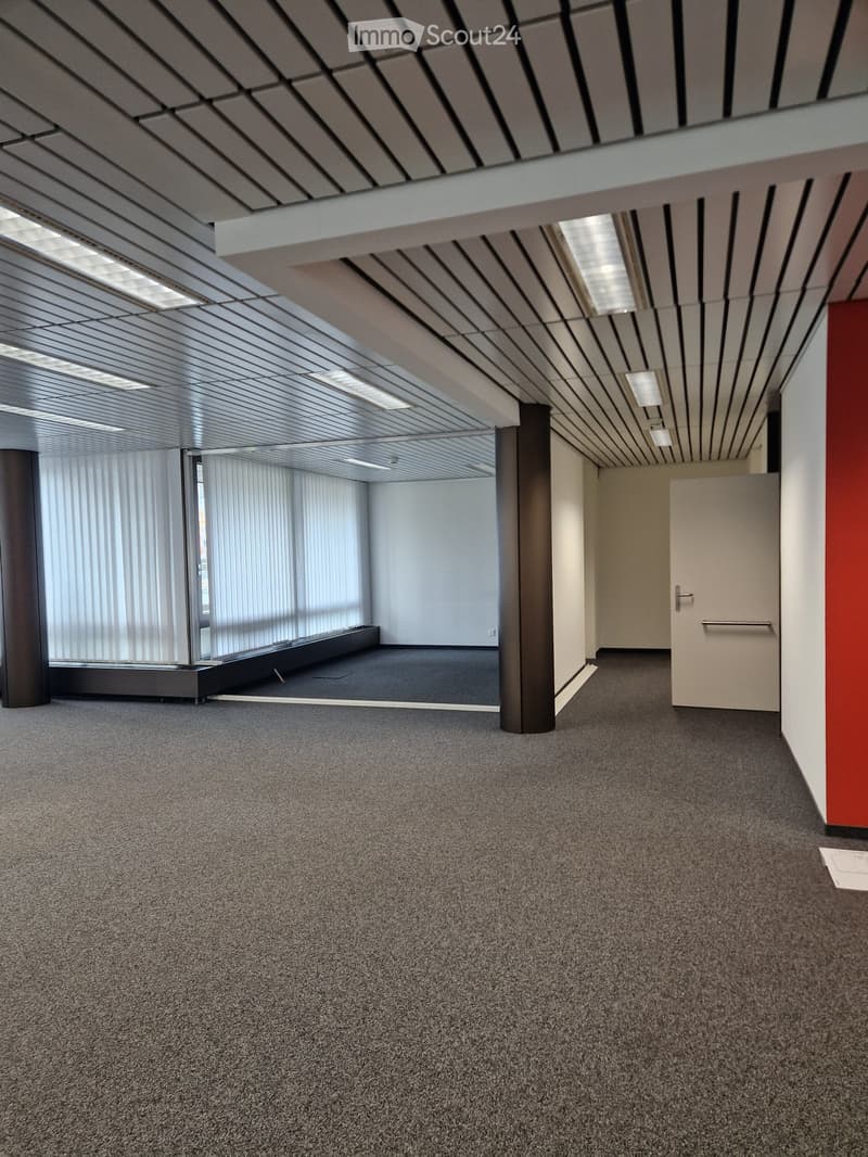 spacious office with white walls, gray flooring, central pillars, vertical blinds, and bright lighting