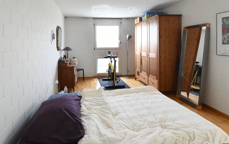 Bedroom with wooden bed, wooden cabinet, floor lamp, mirror, desk with items, and stationary bike.