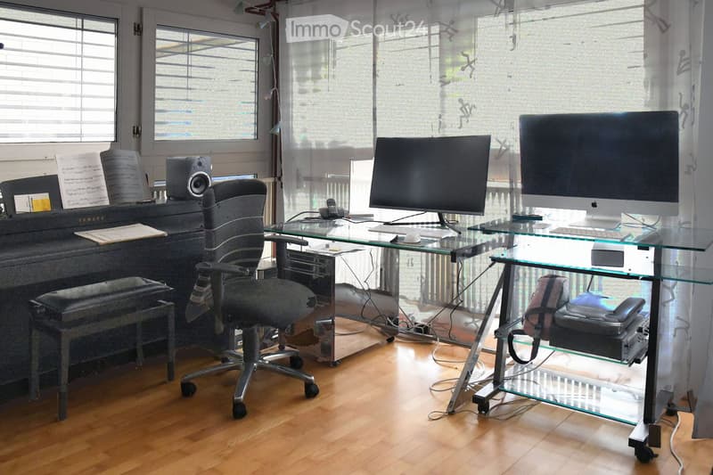 Office with wooden floor, glass desk, office chair, computer monitors, speakers, piano, window, curtain