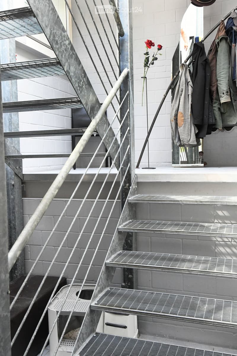 Modern staircase, stainless steel and metal railing, white brick wall, decorative red flower, hanging coat rack with jackets
