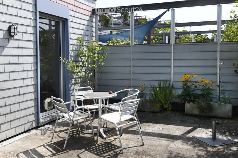 balcony with table and chairs, metal railings, white siding, garden with plants and flowers