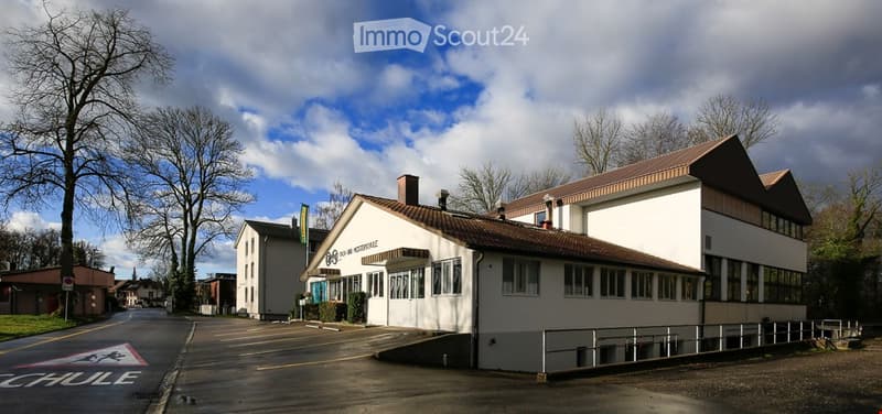 Modern architectural building, white painted walls, brown roof, parking area in front, clear blue sky
