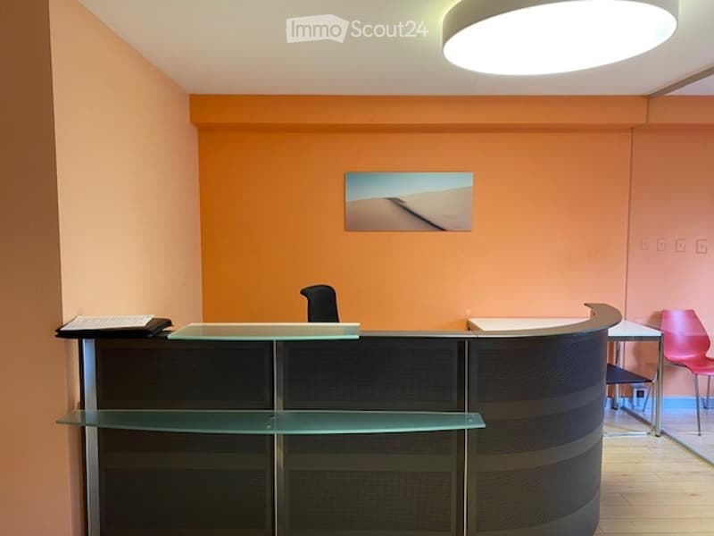 Reception desk, glass shelves, black chairs, modern design, orange and beige walls, picture on wall, desk, round ceiling light