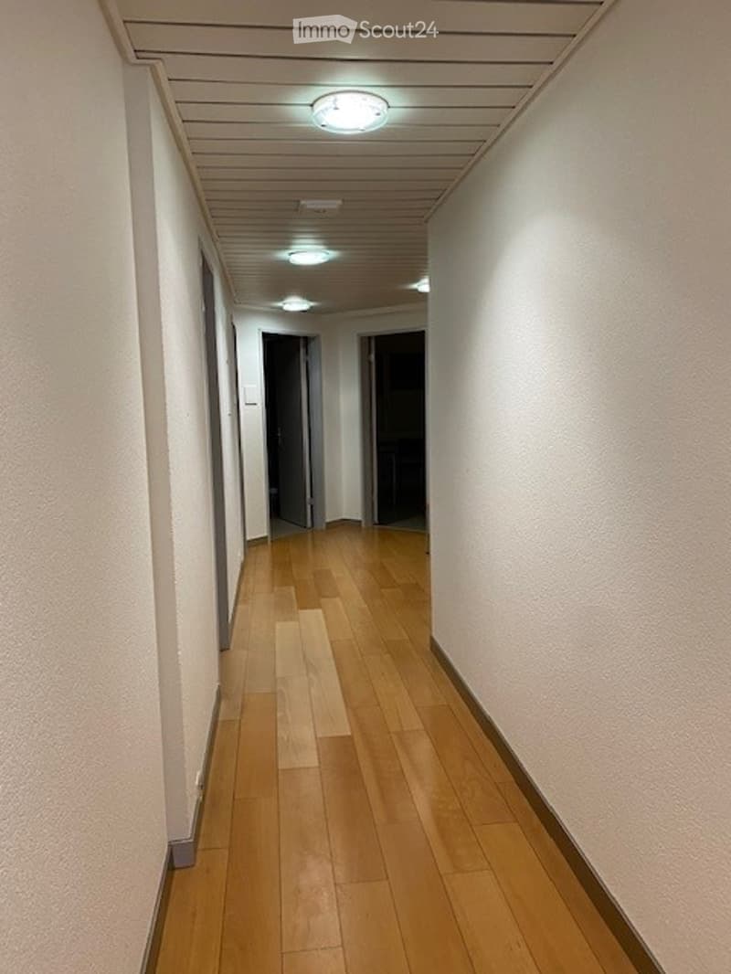 Empty corridor, wooden floors, white walls, two open doors at the end