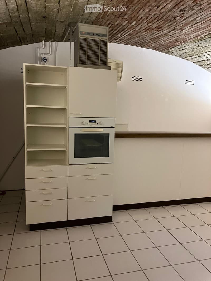 Empty kitchen with white tiles, white cabinets, shelf, and built-in oven, with visible wiring on the wall.