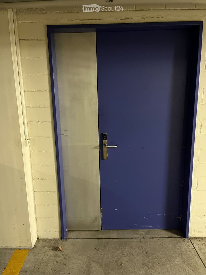 Large blue door with silver handle, concrete floor, white brick walls, yellow line on ground