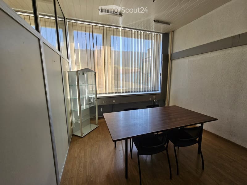 Empty room with a table and chairs, glass display cabinet, window with venetian blinds, wooden flooring, and white walls