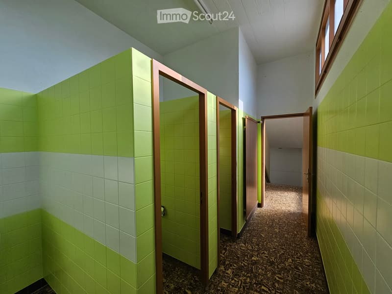 Three green and white tiled walls, two white walls, three cubicles with wooden doors, carpeted floor