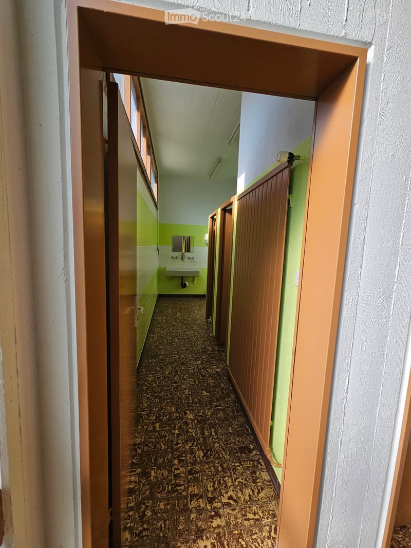 Long hallway with green and white walls, tiled floor, three doors on the right, sink on the wall