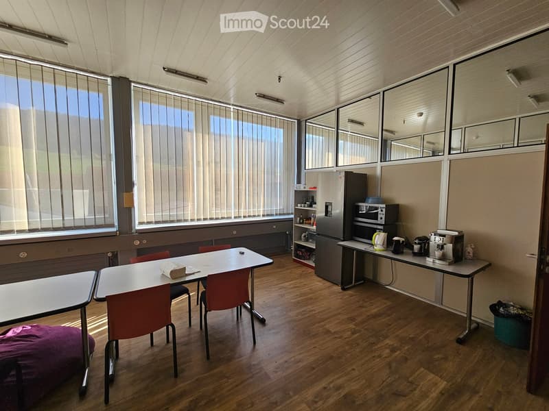Empty room with white walls, wooden floor, windows, kitchen appliances, tables, and chairs.