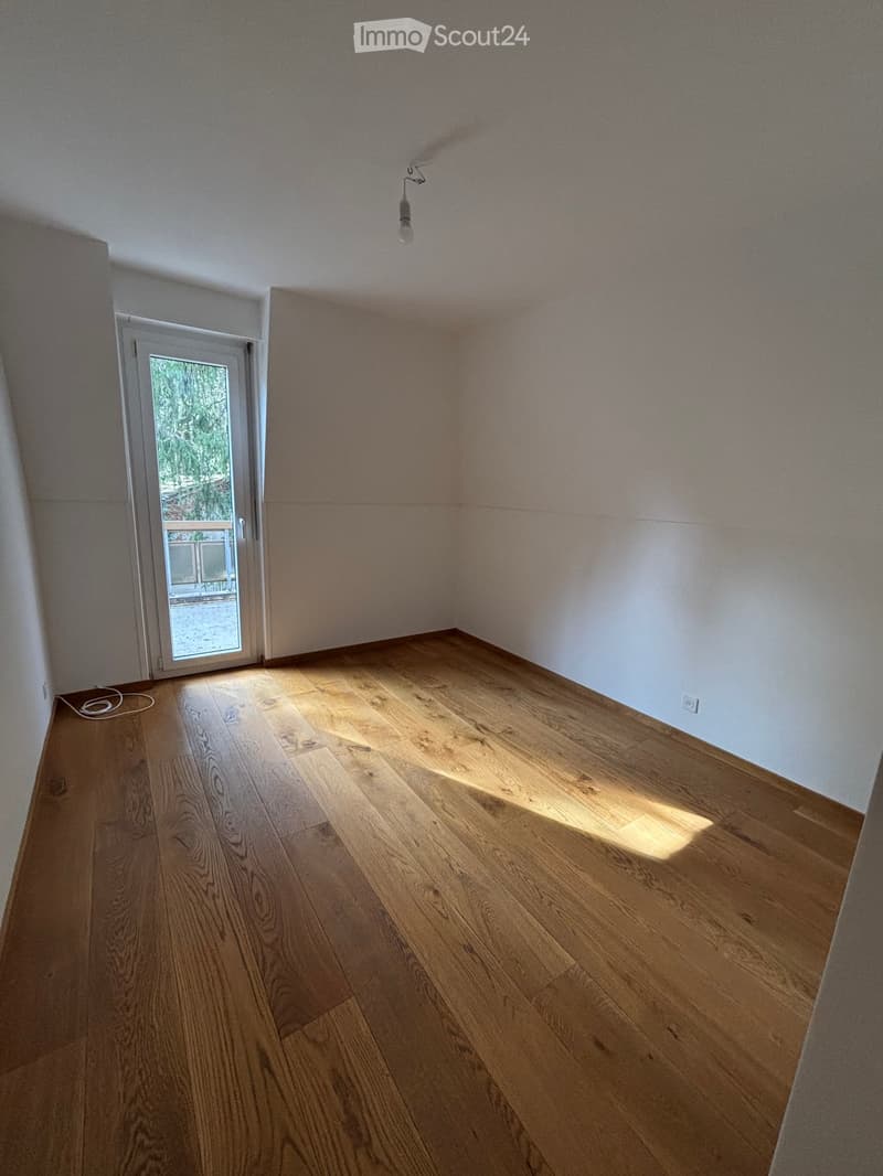large empty room, hardwood floors, white walls, sliding glass door to balcony, power outlet