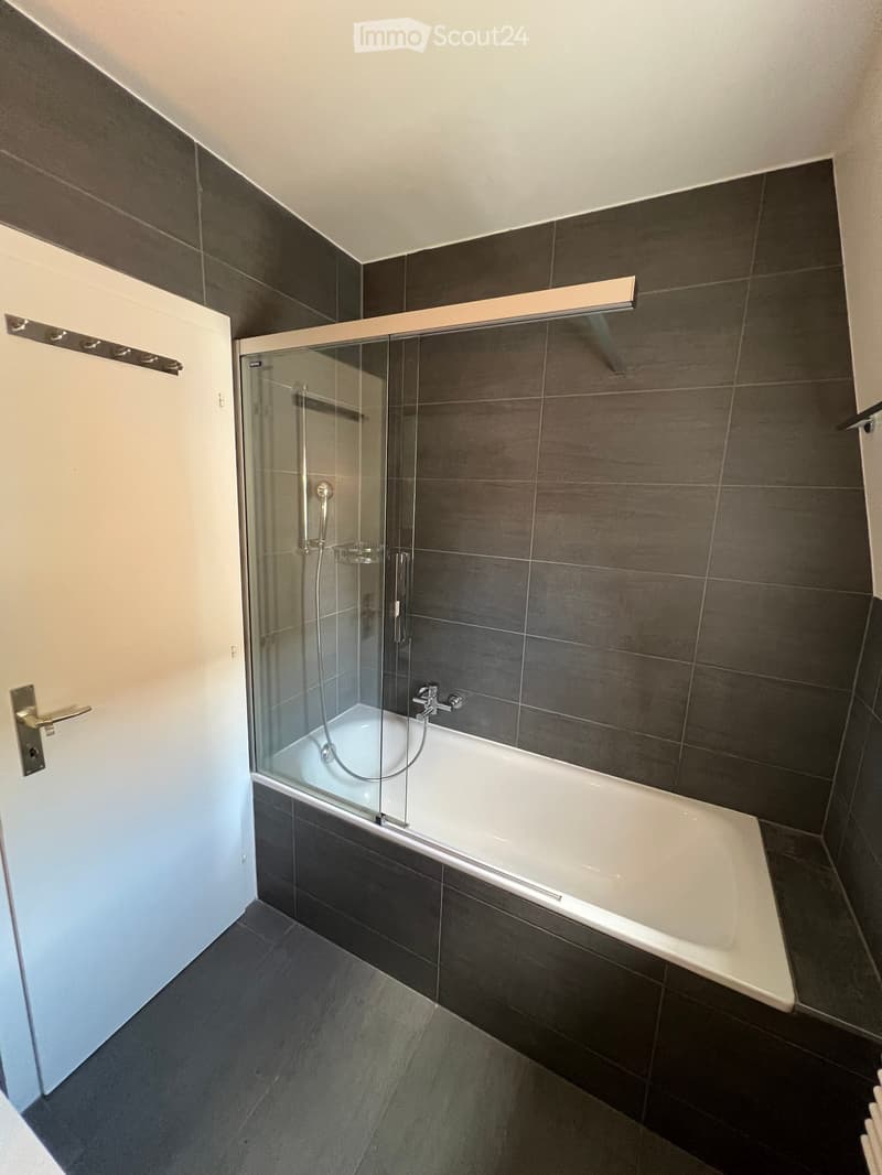 Bathroom with shower, bathtub, grey tiles, white bathtub