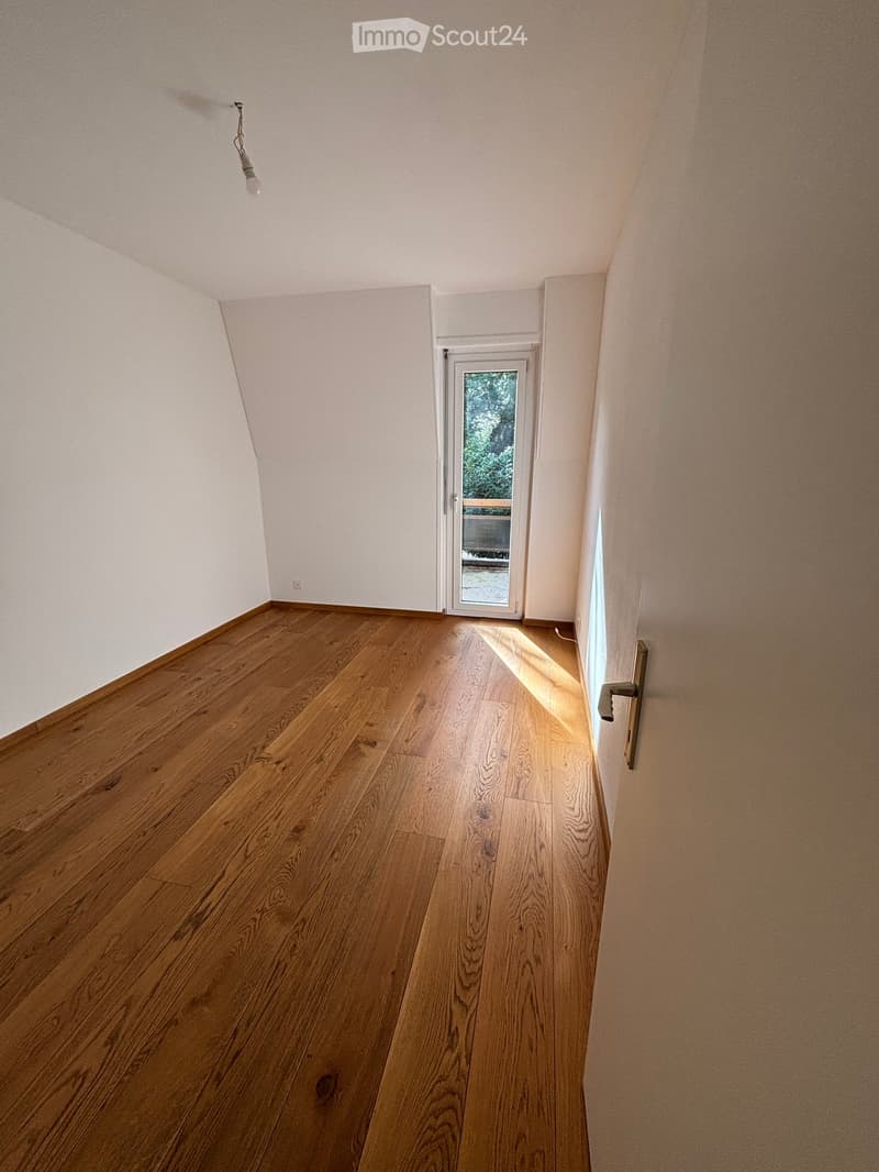 Empty room with wooden floors, white walls, a balcony with glass doors, and a white door.