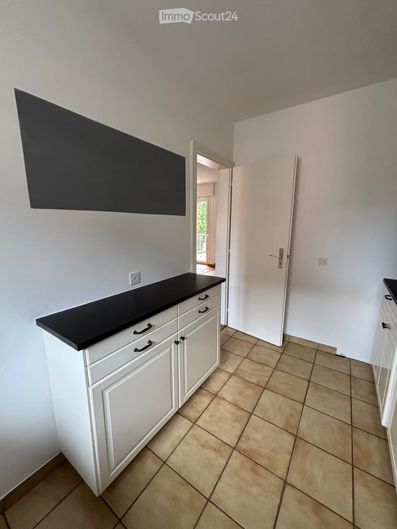 A kitchen with white cabinets, a black countertop, tiled floor, and a power outlet mounted on the wall.