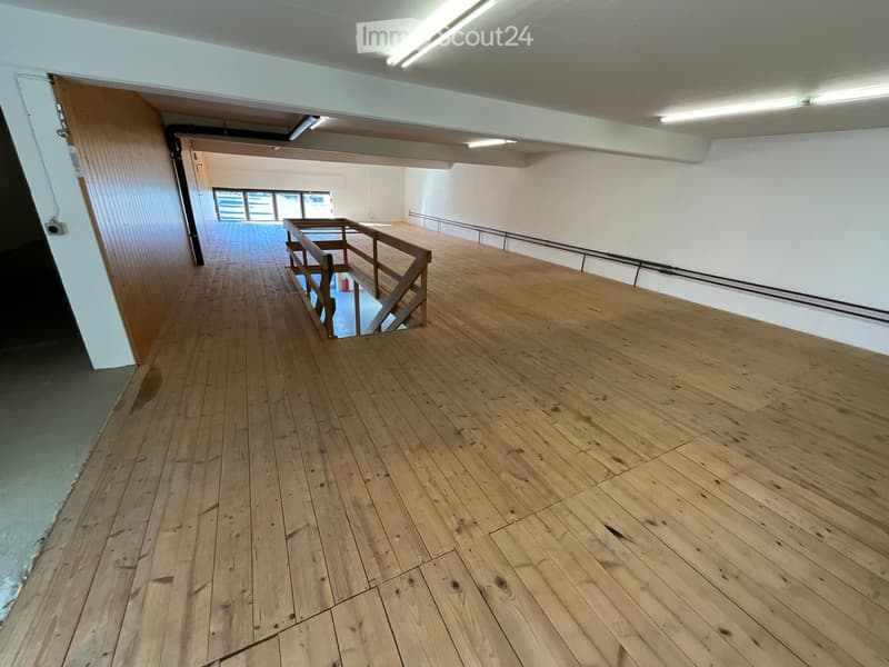 Empty room with hardwood floors, wooden railings, metal pipes along the wall, and white walls